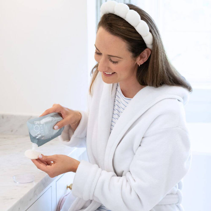 AO2 Clear - Acne Clearing - 30 Day Kit being applied with a sponge by a woman in a white robe at a bathroom counter.
