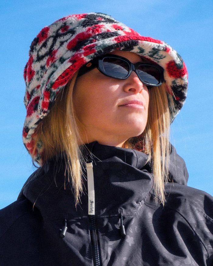 Person wearing a colorful patterned hat and black sunglasses against a blue sky.