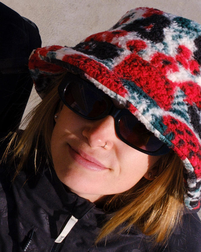 Person wearing a colorful knitted hat and sunglasses with a neutral background