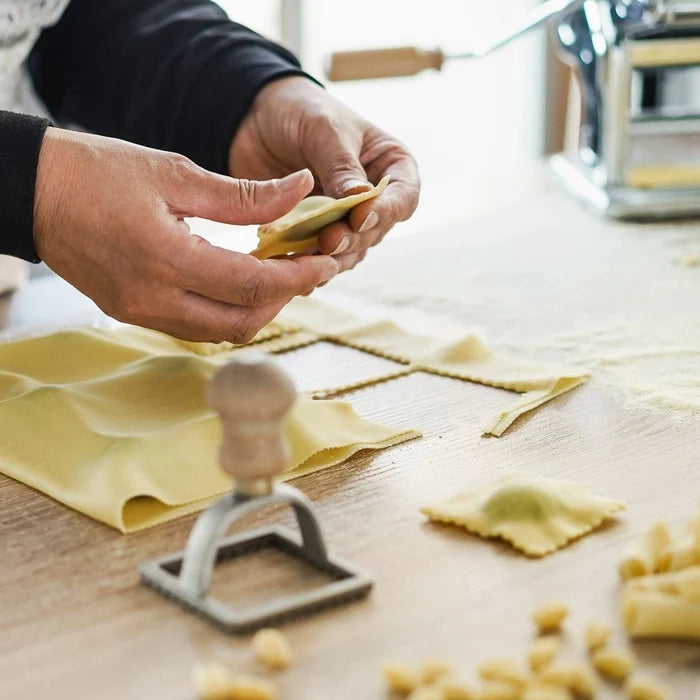 Person making ravioli with a pasta press on a wooden surface